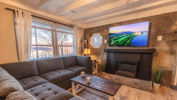 Una sala de estar con un sofá modular, una mesa de centro de madera, una chimenea y un televisor grande montado en una pared de piedra.