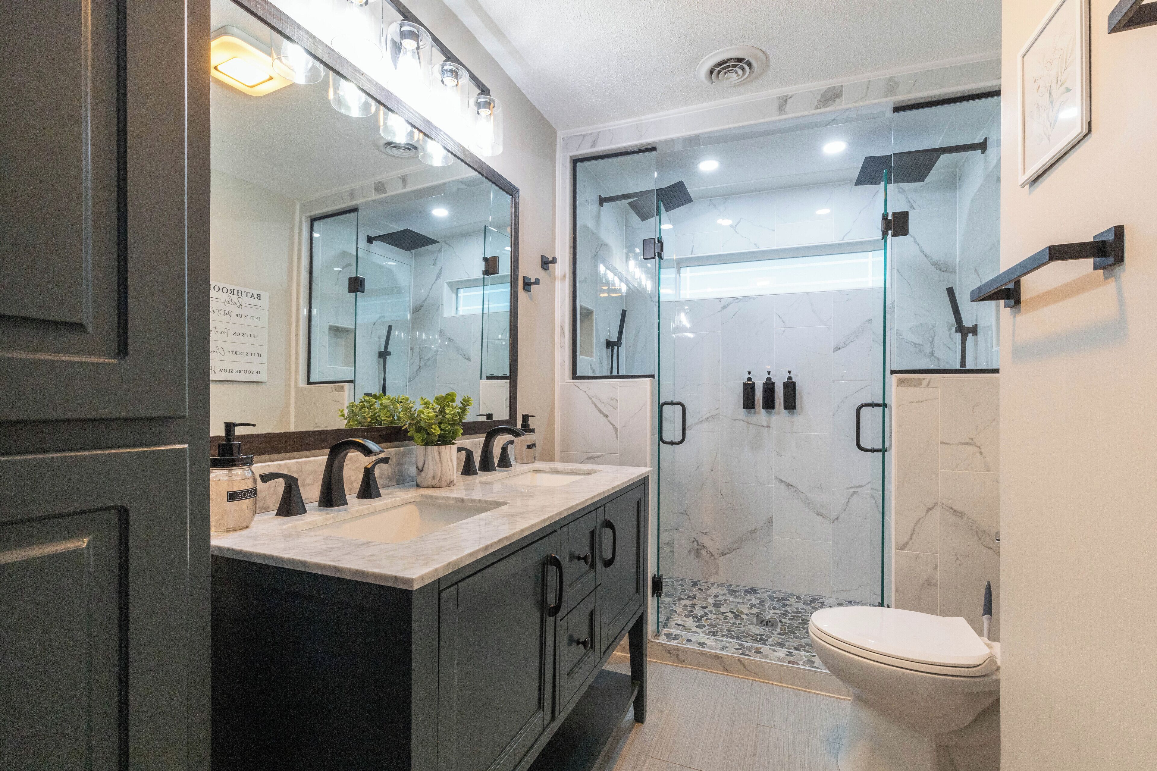 Een moderne badkamer met een marmeren wastafel, zwarte kastjes, een glazen douchecabine en een toilet.