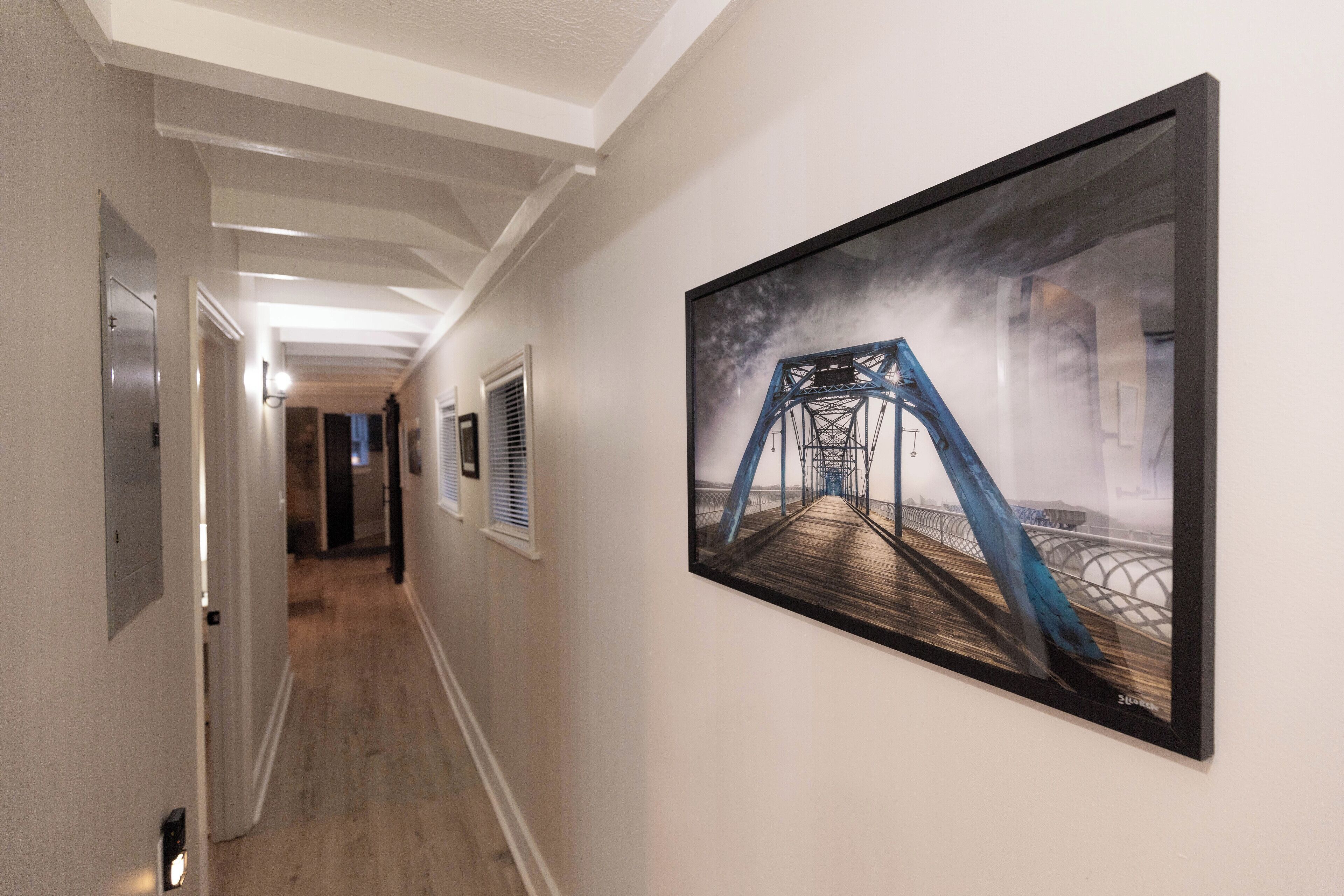 A hallway with a framed artwork of a bridge, a door, and a vent.