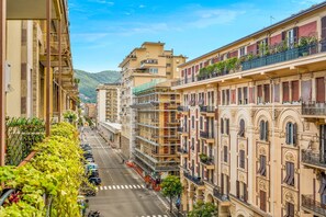 Une vue d’une rue de ville, avec des immeubles à plusieurs étages, dont certains sont dotés de balcons et de plantes.