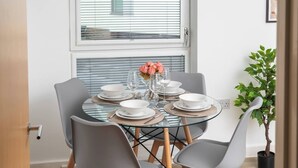 A dining area with a round glass table set for four, surrounded by grey chairs with wooden legs. - Beautiful Flat • Prime Location • Balcony • Free Parking • Self-Check-In (Milton Keynes)