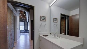 Un baño moderno con un espejo grande, muebles blancos y suelo de madera.