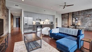 Una sala de estar moderna con un sofá azul, una mesa de centro y una zona de comedor con una pared de ladrillo.