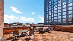 Terraza en la azotea con piso de madera y mobiliario exterior, con vista a un paisaje urbano.