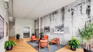 Un vestíbulo espacioso con pared de ladrillo, piso de madera y varias zonas de estar con cojines naranjas.