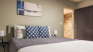 Una camera d'hotel con un letto, un quadro appeso alla parete e un muro in mattoni visibile attraverso una porta aperta.