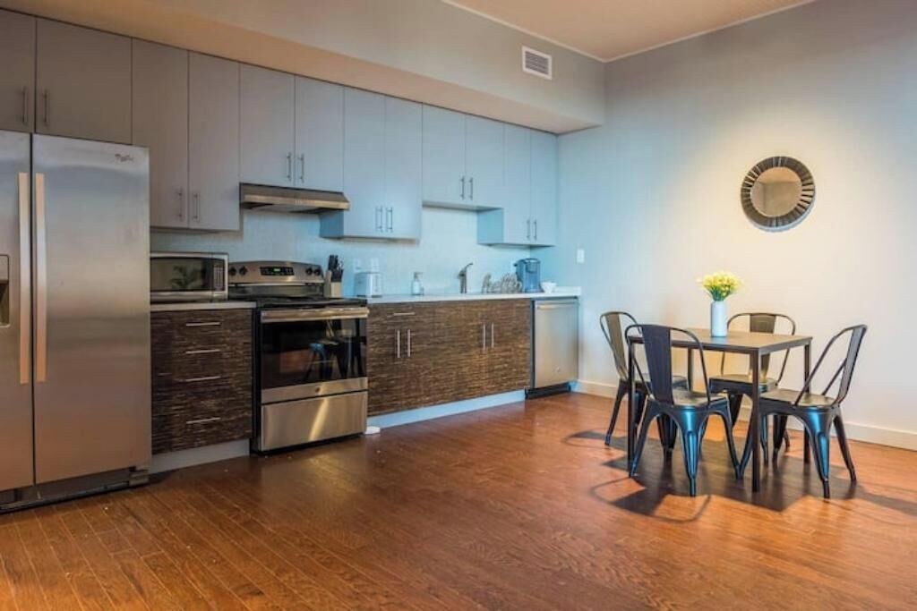 A modern kitchen with stainless steel appliances, wooden cabinets, and a dining area with metal chairs.