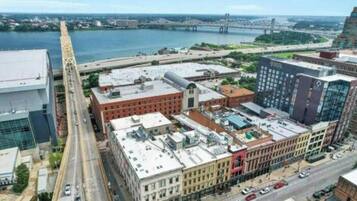 An aerial view of a cityscape with a river, a bridge, and various buildings including a large red brick building and a modern glass building.