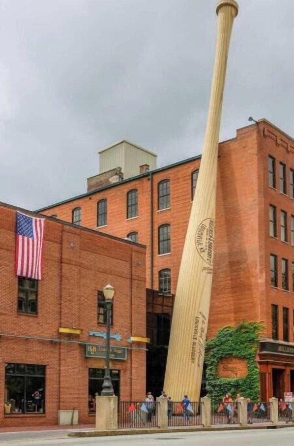 Un bate de béisbol alto color beige apoyado contra un edificio de ladrillo con una bandera estadounidense.