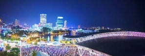 A large outdoor event with a crowd, a stage, and a city skyline in the background.