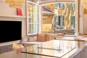 A modern interior with a dining area, a sofa, and a view of a building with green shutters.