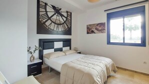 A bedroom with a bed, a nightstand, a wall clock, a window, and a painting.