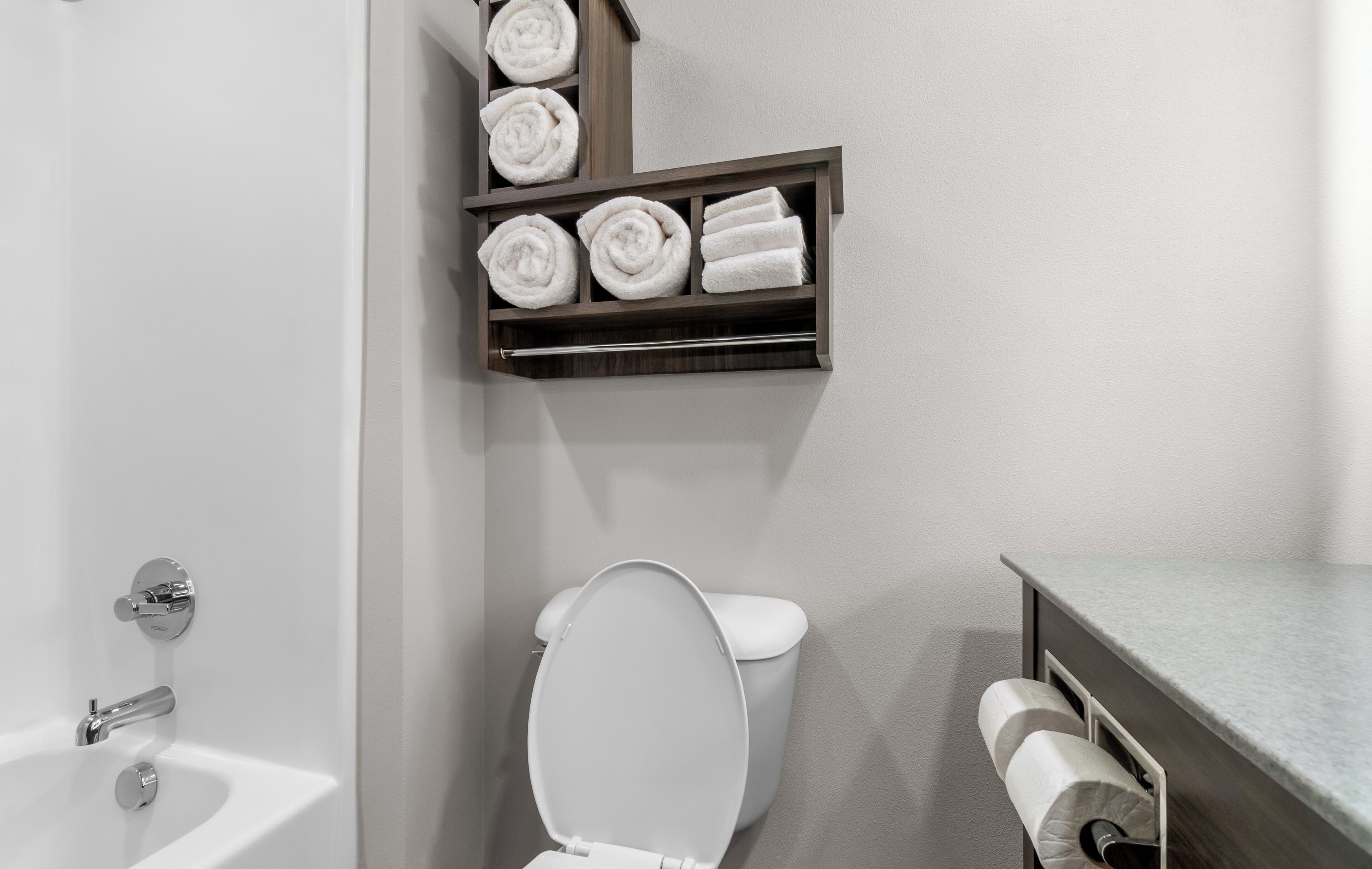 Une salle de bain avec des toilettes blanches, un lavabo et un porte-serviettes sur lequel sont soigneusement pliées des serviettes.