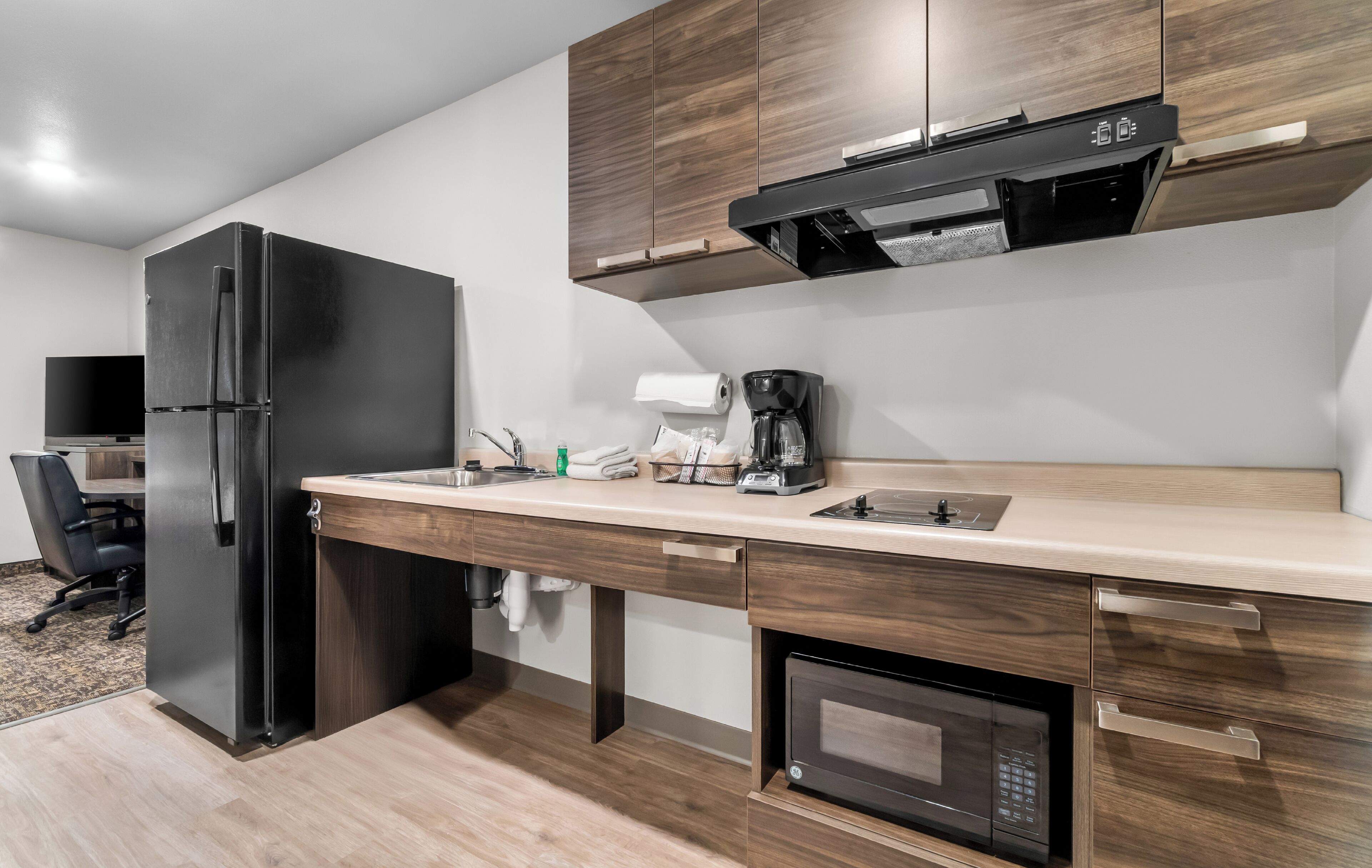 A modern kitchen with a refrigerator, microwave, coffee maker, and wooden cabinets.
