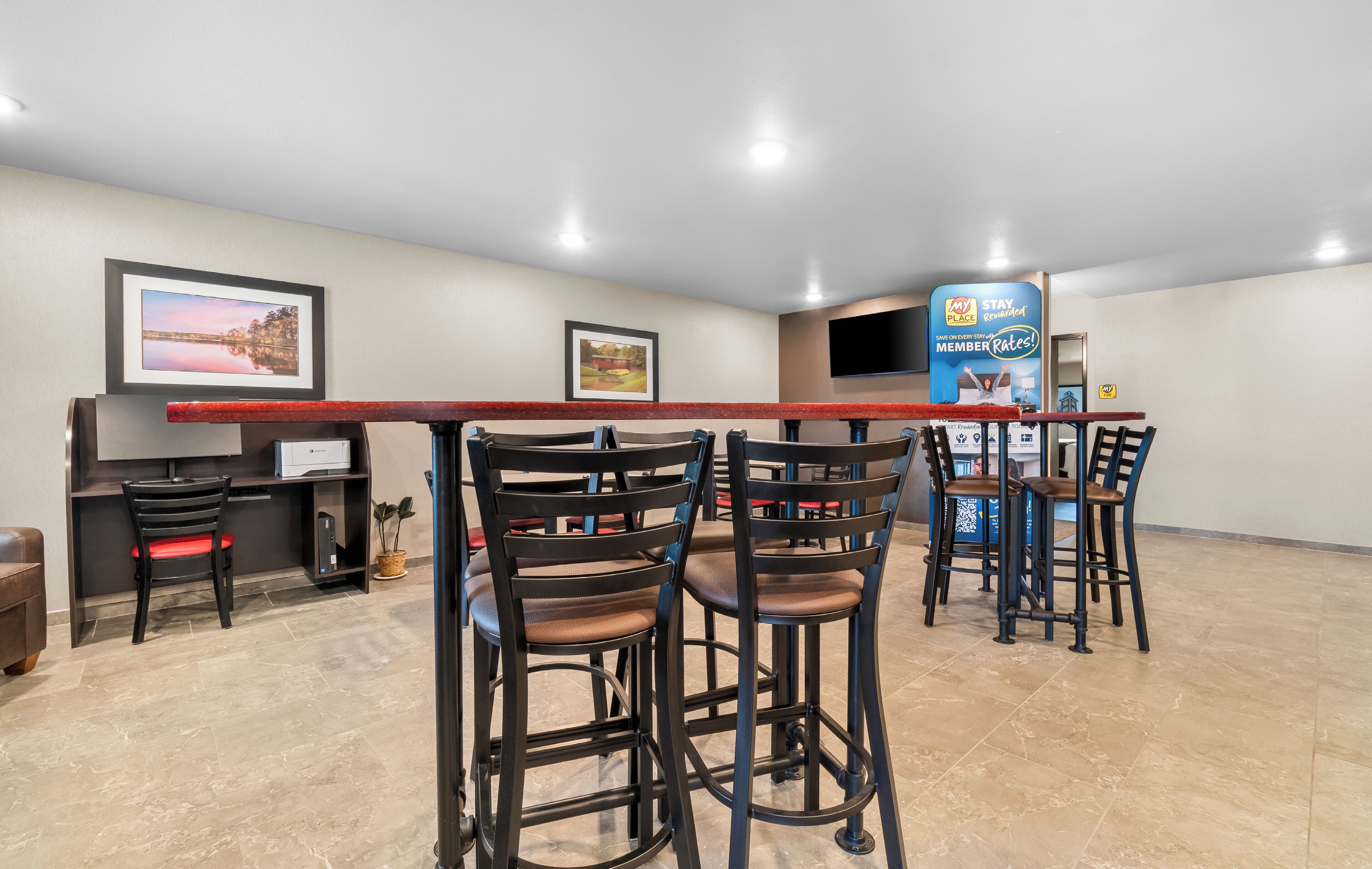 A bar area with high stools and a long counter, a television mounted on the wall, and framed pictures on the walls.