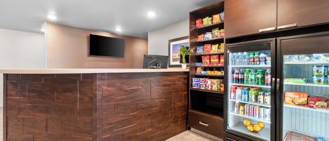 A reception area with a wooden reception desk, a flat-screen TV mounted on the wall, and a beverage refrigerator stocked with drinks and snacks.