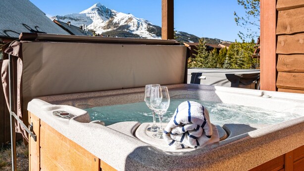 A wooden hot tub with a towel and glasses, set against a mountain backdrop. - Big Sky Ski Chalet 3 Mins to Lifts with Hot Tub, Fireplace & Queen Bed Bunk Room (big sky)