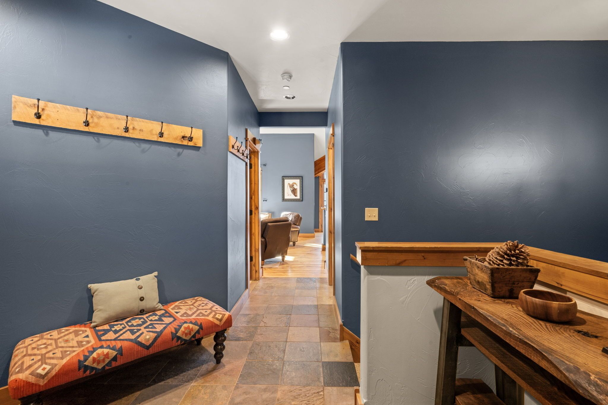 A hallway with a bench, a coat rack, and a wooden table with a pinecone and bowl.
