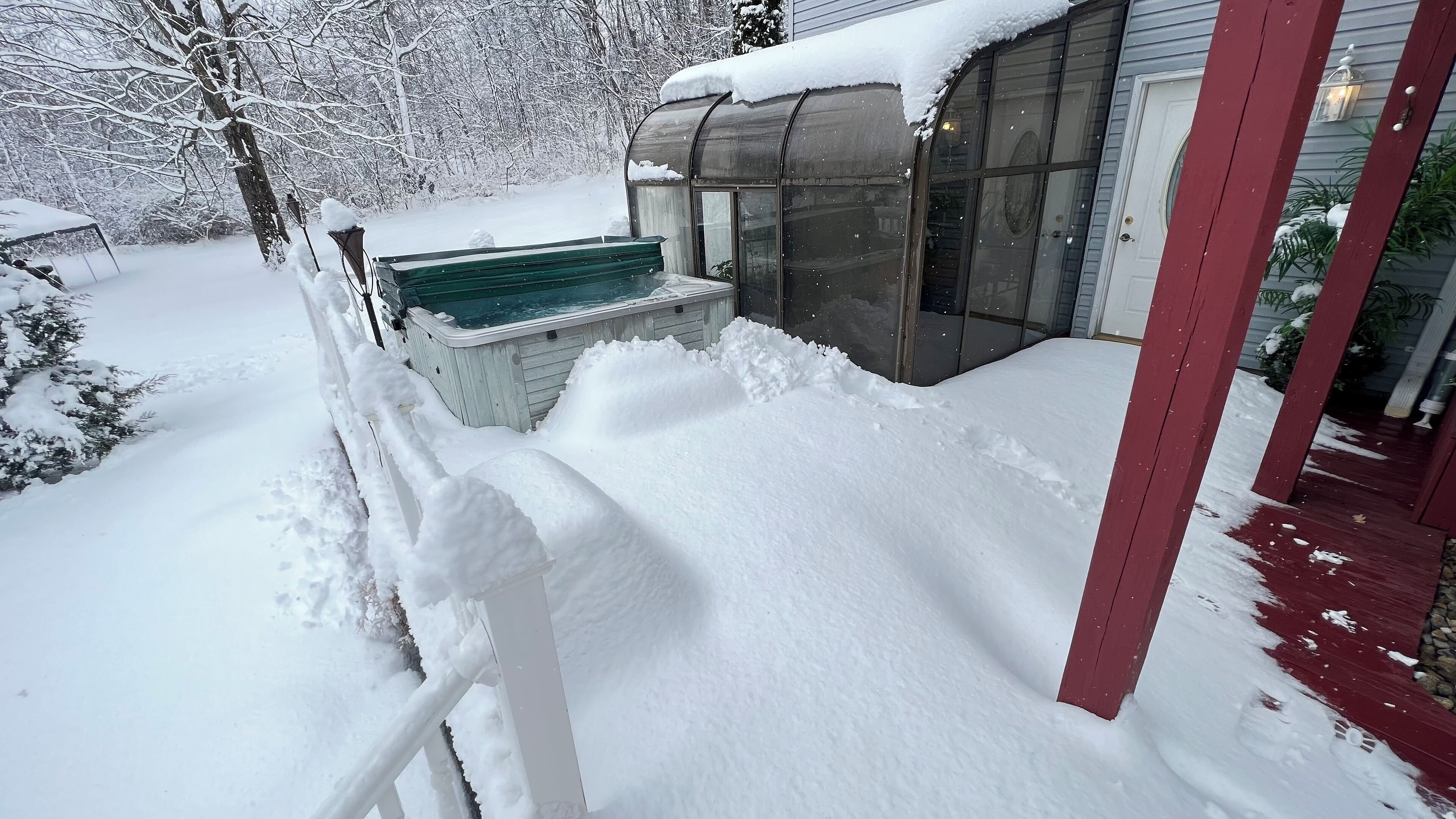 A snow-covered porch with a hot tub and a greenhouse.