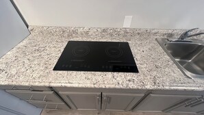 Una cocina con cocina por inducción negra, encimera de granito, pileta de acero inoxidable y muebles de madera.