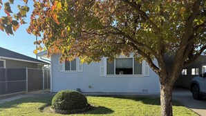 Una casa residencial con un césped cuidado, un árbol pequeño y un patio cercado.
