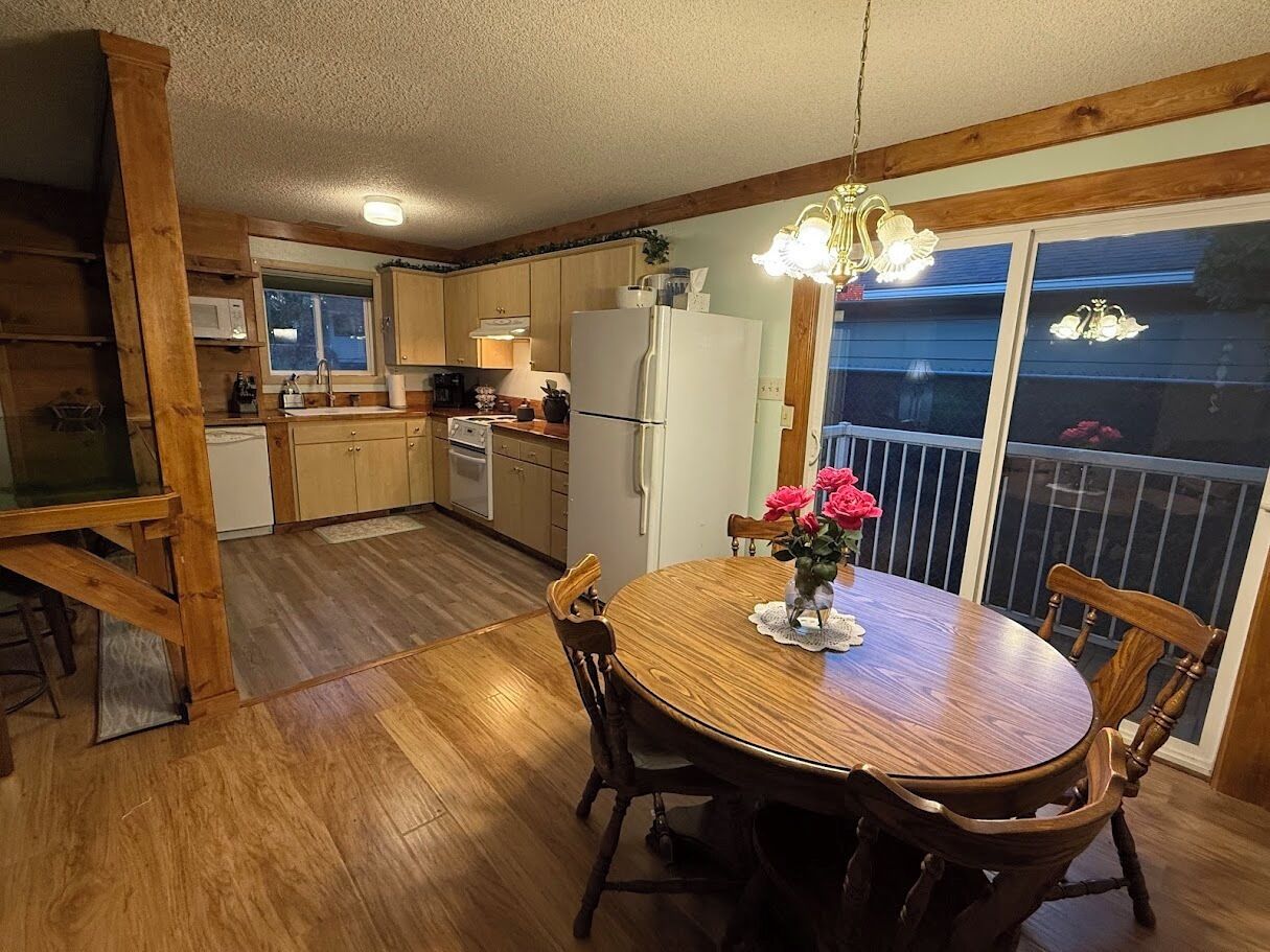 Une cuisine avec des meubles de rangement en bois, une table à manger avec des chaises et un balcon doté d’une balustrade.
