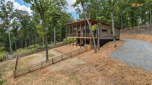 A two-story cabin with a wooden exterior, surrounded by a wooden fence and trees.