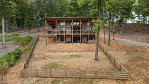 A two-story wooden cabin with a deck, surrounded by trees and a fenced yard. - Modern Rustic Log Cabin-Dog Friendly-Fenced-Views-Hot Tub (Morganton)