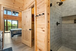 A wooden interior with a bed, a shower area, and a view through a large window. - Modern Rustic Log Cabin-Dog Friendly-Fenced-Views-Hot Tub (Morganton)