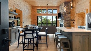 A modern kitchen with wooden walls, a stone accent wall, and a large island with seating. - Modern Rustic Log Cabin-Dog Friendly-Fenced-Views-Hot Tub (Morganton)