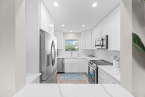 Cocina moderna con armarios blancos, electrodomésticos de acero inoxidable, una ventana y una alfombra azul.