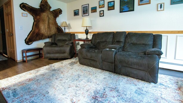 A living room with a large bear hide mounted on the wall, a grey sofa, a patterned rug, and several framed pictures on the wall.