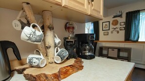 A kitchen with a rustic decor, including a coffee maker, mugs, and a wooden cutting board.