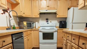 A kitchen with wooden cabinets, a stainless steel dishwasher, a white stove, and a refrigerator.