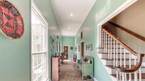 A hallway with a staircase, a bench, and a decorative wall hanging.