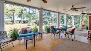 A covered patio with outdoor furniture, ceiling fans, and a view of the surrounding trees.