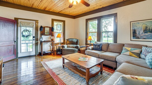 A spacious living room with a wooden ceiling and hardwood floors, a large sofa, a coffee table, and a fireplace. - Walk to Downtown: The Porch Swing Cottage (Winnsboro)