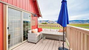 A covered patio with a wicker sofa and table, a blue umbrella, and a view of distant mountains. - Mtn & Golf Course View: Oregon Outback Getaway! (Lakeview)