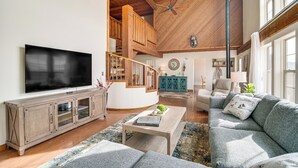 A spacious living room with a large flat-screen TV, wooden staircase, and a cozy seating area with a sofa and armchair. - Mtn & Golf Course View: Oregon Outback Getaway! (Lakeview)