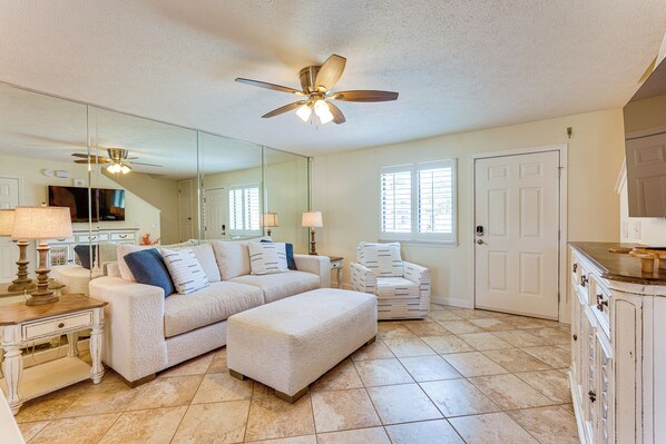 A spacious living room with a large sectional sofa, a matching ottoman, a white armchair, and a dining area with a cabinet and a television. - Relax Poolside & Walk to Beach! Resort PCB Retreat (Panama City Beach)