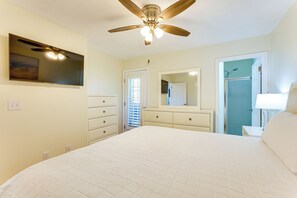A bedroom with a large bed, a ceiling fan, a dresser, a mirror, and a door leading to another room. - Relax Poolside & Walk to Beach! Resort PCB Retreat (Panama City Beach)