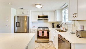 Een moderne keuken met roestvrijstalen apparatuur, witte kastjes en een betegelde vloer.
