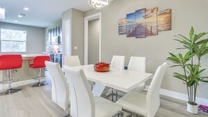 Un espace repas moderne avec une table blanche, des tabourets de bar rouges et une plante en pot.