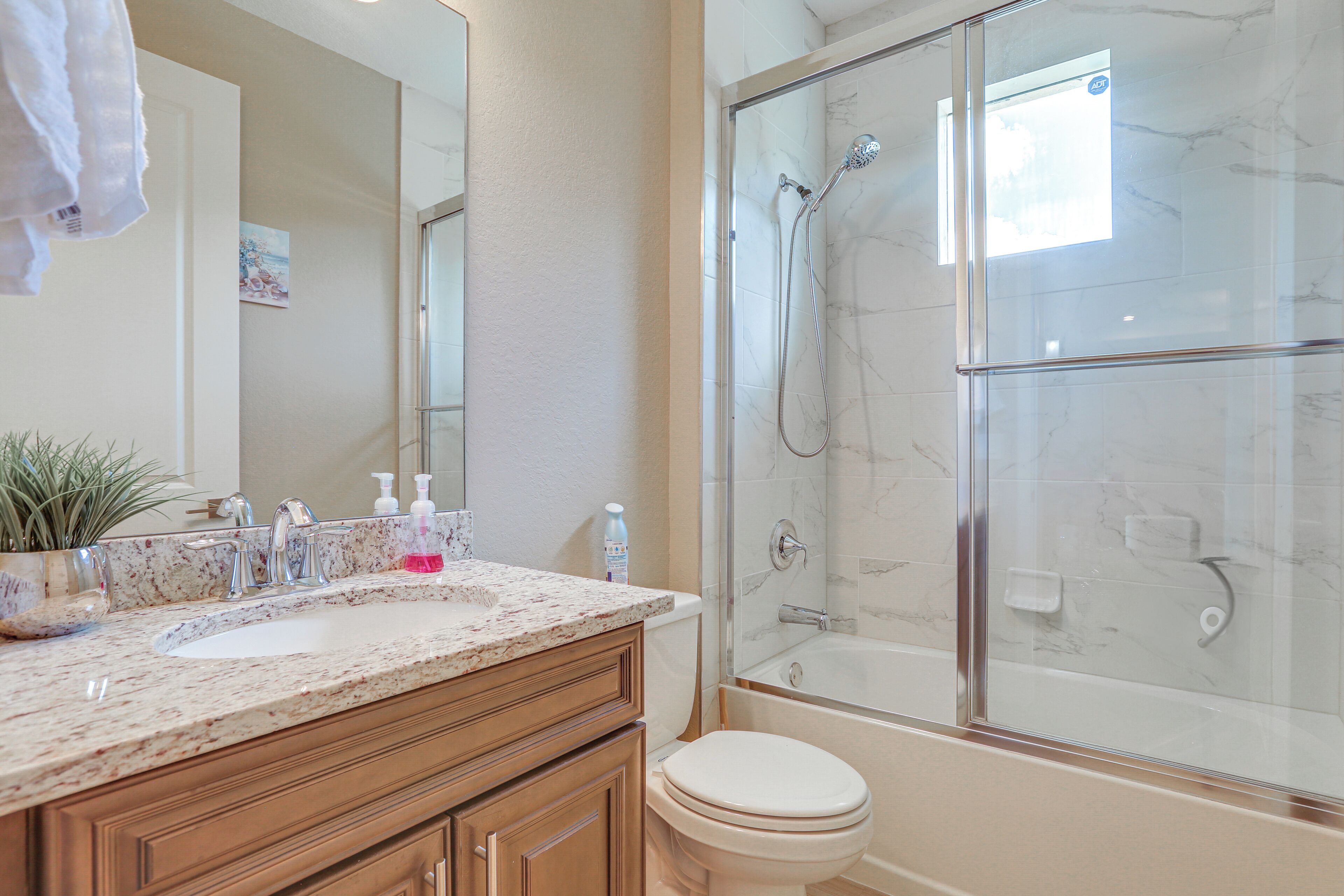 A bathroom with a marble sink, wooden cabinets, a toilet, and a glass-enclosed shower.