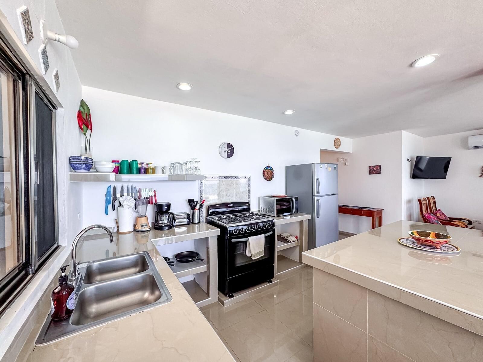 Una cocina moderna con estufa a gas, microondas y refrigerador. Hay un lavamanos con grifo y una ventana con vistas al exterior.