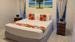 Une chambre avec un grand lit, un ventilateur de plafond et deux tableaux accrochés au mur.