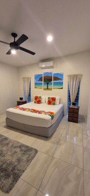 Een slaapkamer met een groot bed, een plafondventilator en twee schilderijen aan de muur.