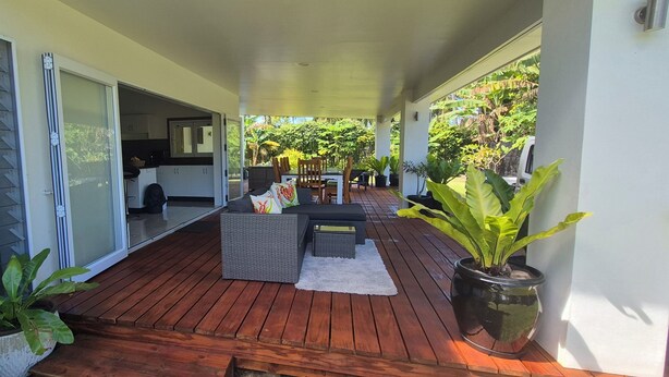 Une terrasse couverte avec une plateforme en bois, un coin repas avec une table et des chaises, et des plantes en pot.
