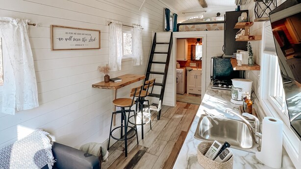 A cozy cabin interior with a dining area, kitchen, and a loft bedroom.