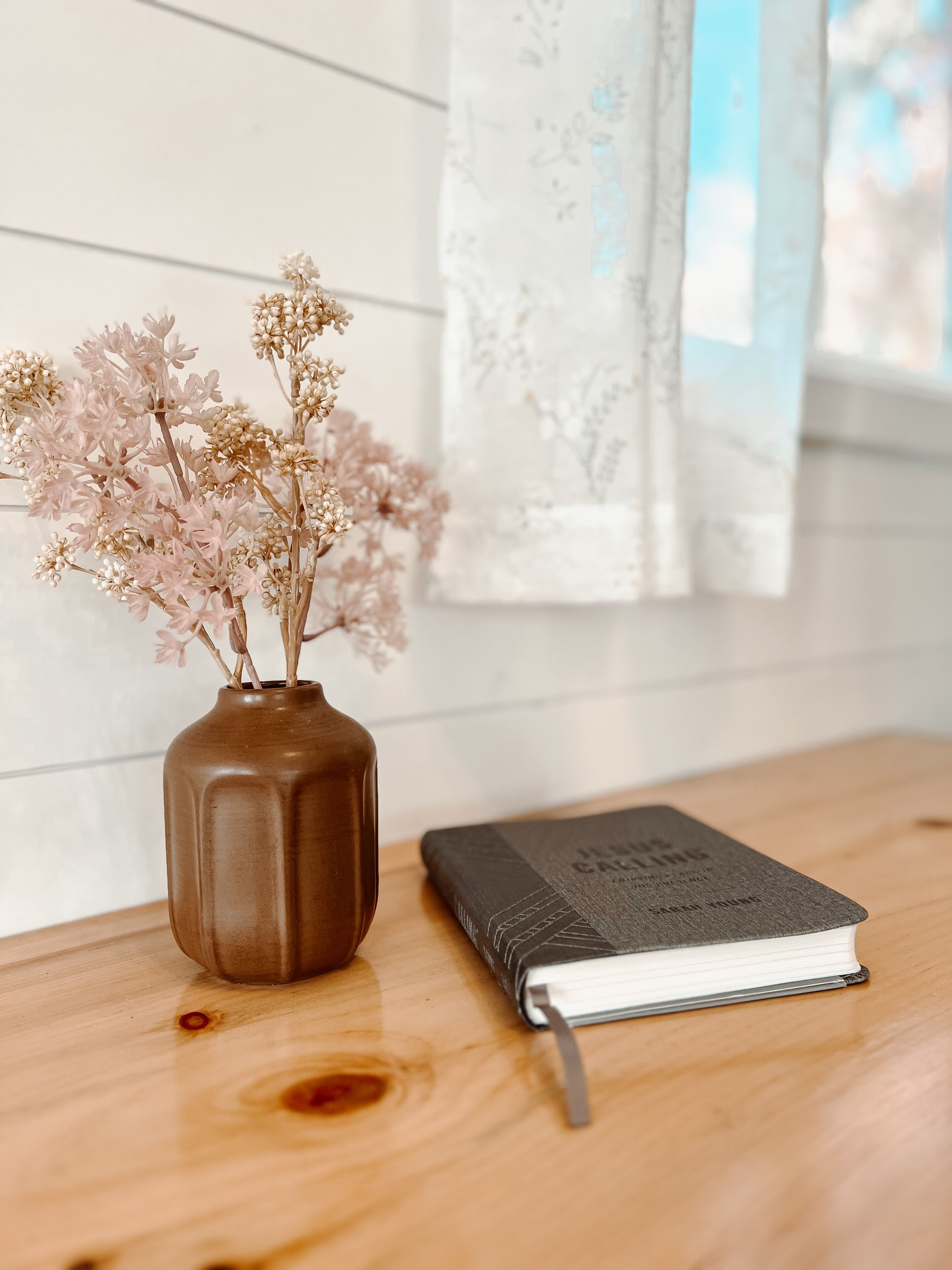 A wooden table with a vase of dried flowers and a closed book.